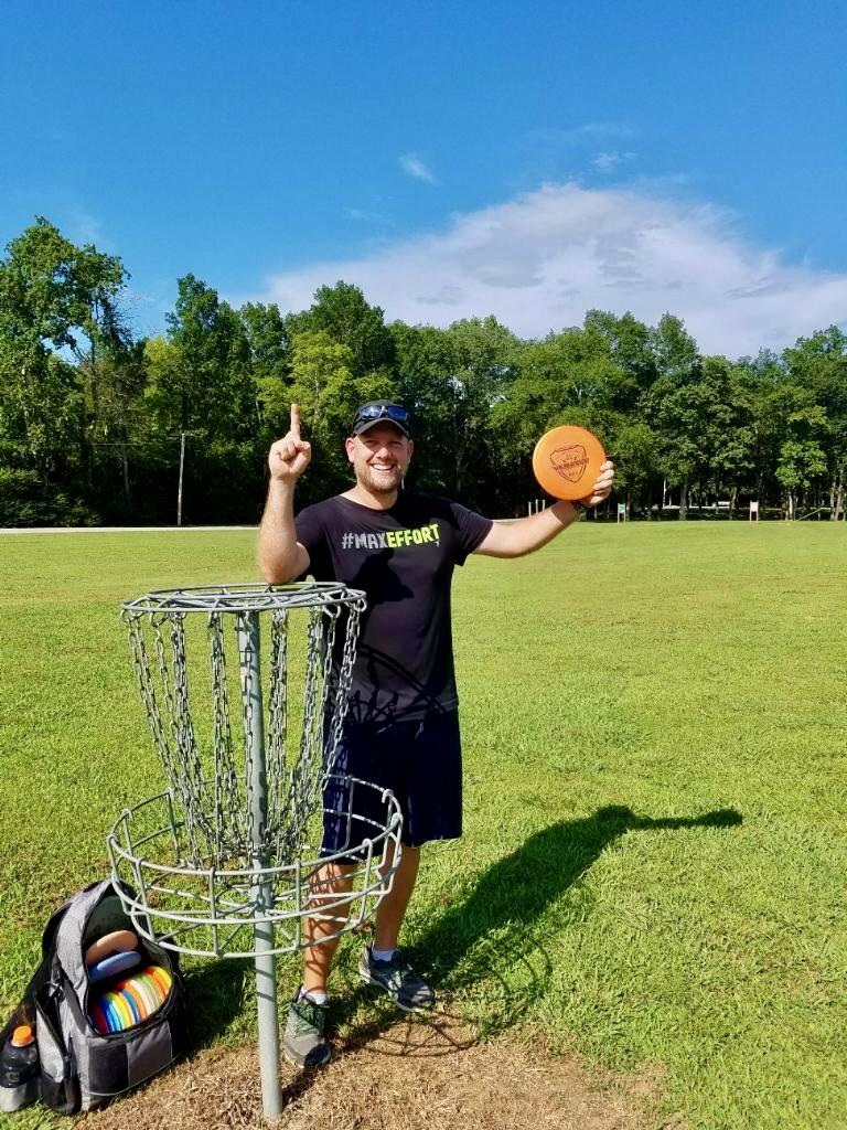 Jason Skipper celebrating his first ace (hole-in-one) in disc golf at Shelbyville, Tennessee, holding the disc near the basket on a bright, sunny day.