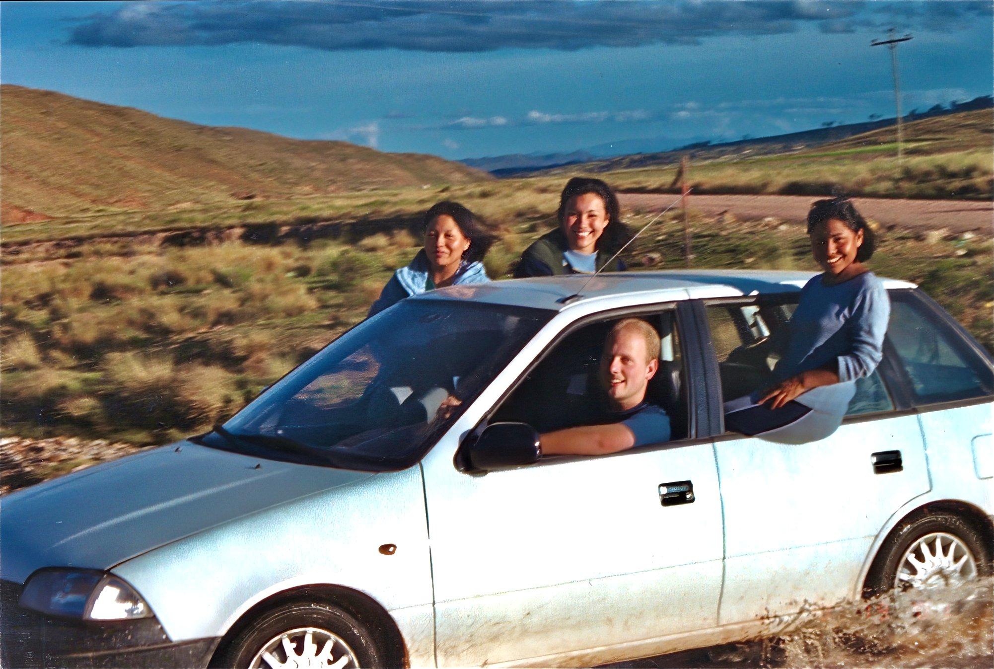 Jason driving through a shallow stream in Bolivia with Norah and two friends riding with the windows down and enjoying the scenery.