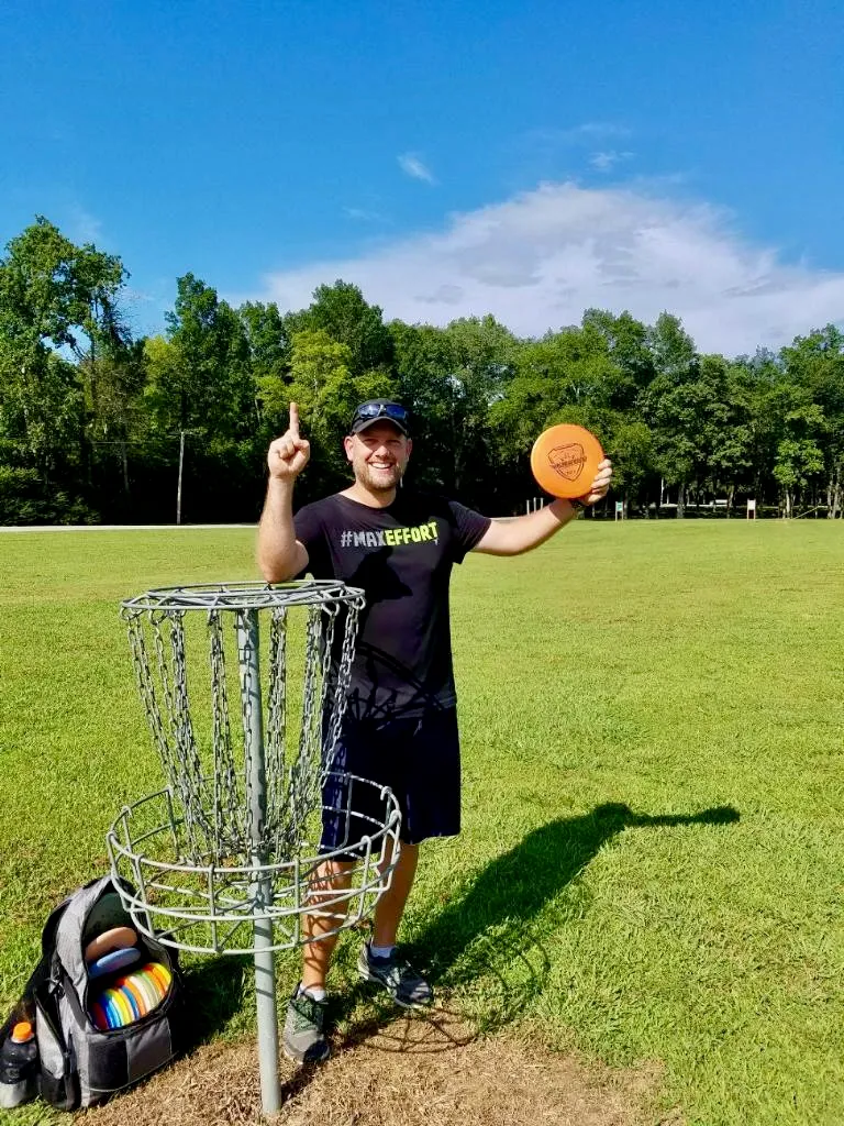 Jason Skipper celebrating his first ace (hole-in-one) in disc golf at Shelbyville, Tennessee, holding the disc near the basket on a bright, sunny day.